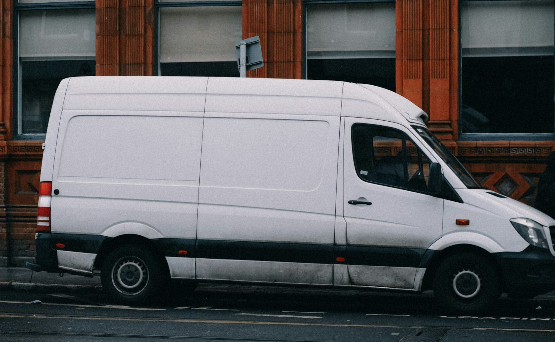 Witte bestelbus geparkeerd langs een stoep voor een bakstenen gebouw